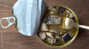 Using fork takes a sardines fish, sardines in oil sauce from a tin can. Top view, close up, macro