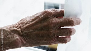 Old elderly lady with wrinkled hand opening curtains to look outside. Situation of poorness and loneliness among elderly people. Stock Video