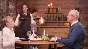 Young waitress brings food to senior couple at date. Serving food to an old couple in a vintage restaurant.