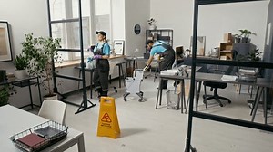 Zoom arrière photo de deux personnes multiethniques en uniforme à l'aide de l'équipement de nettoyage et de la prudence S'identifier espace de bureau moderne