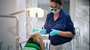 Woman sitting on dental chair, conversation with dentist. Dental clinic doctor in cabinet talking and gesticulate, explaining, preparing patient for treatment. Rear view of patient, focus on dentist.