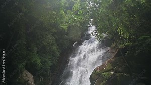 Stunning slow motion scene of waterfall in tropical rainforest during rainy season. Water strong falling from high rocky cliff surrounded by green plants in the forest. Ton Sung Waterfall, Thailand.