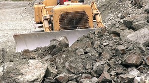 Front view of bulldozer in action,moving rocks towards the camera in a high angle static shot witness the power and precision of this heavy machinery.