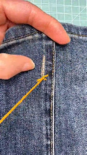 sewing a small cross stitch using a bright yellow thread onto a blue denim fabric surface today ya