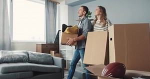 Moving to new apartment of young couple in love. Happy couple stroking dog. Cheerful playful dog licking the owners. People laughing.