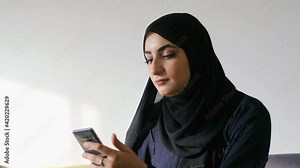 Arab woman using mobile app on her smart cellular phone. Middle Eastern girl wearing Abaya Hijab hair scarf for Emirati women texting
