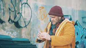 A Homeless Man is Eating Food From a Trash Bin