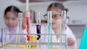4K, Close-up of colored science test tubes with a blurry background of two children having fun mixing colors in a school lab. Concept education, Science experiments, Chemistry and Children