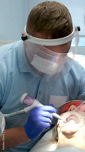 Close-up face male dentist black mask his face work. surgeon saws bone, performs operation with nurse, assistant. Dentist surgeon nitrile gloves removes complex wisdom tooth.