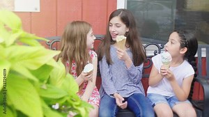 Girls on Bench Eating Ice Cream. a slow motion move right on three girls eating ice cream on a bench talking