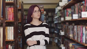 Young woman standing between bookshelves in a library - Free Stock Video