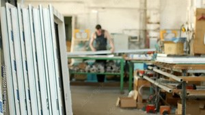 The production of assembly and manufacturing of PVC windows, a workshop with finished products, in the background, a worker measures the PVC profile for further assembly of the PVC window, workshop