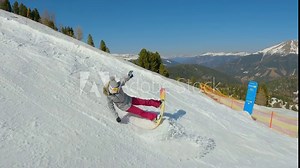 Girl snowboarder falls back on snow while learning to snowboard on ski slope. Young woman landing in snow after losing balance while snowboarding down the piste at snow-covered mountain ski resort.