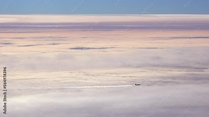 Airplane seen in silhouette with contrails in front of pink sunset clouds.