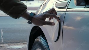 African male hand inserts power connector into EV car near the road in winter. Unrecognizable african man plugging in charging cable to electric vehicle and charges batteries