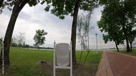 a woman in black walks past a white trash can, throwing some trash into it as she goes