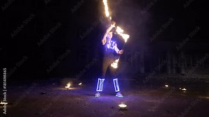 Fire show performance. Handsome male fire performer twirling and tossing up fire baton staff ignited from both sides.