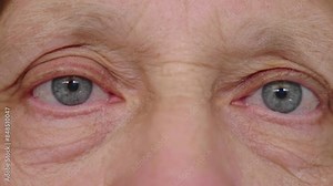 Close-up shot of a mature woman with long blonde/brown hair, focusing on her very blue eyes. The detailed view highlights the intensity and depth of her gaze.