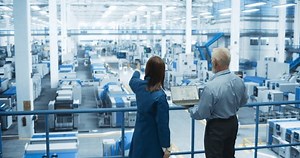 Middle Aged Engineer and Young Japanese Technician Having a Conversation and Using Laptop Computer. Specialists Monitoring, Analyzing Conditions at a Modern Electronics Factory with Automated Robots