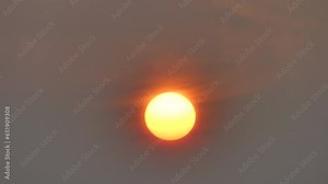 Grey and red sky around yellow solar disk with Atmospheric refraction during sunrise - sun with distorted shape caused by atmospheric optical phenomenon. In real time on misty winter weather.