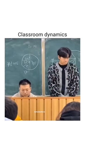 LOL on Instagram: "The video, titled "Classroom dynamics," captures a humorous and relatable moment between a male student and his teacher. The scene is set in a typical classroom with a large green chalkboard in the background covered in mathematical pie charts and equations. A young man, wearing a trendy black and white leopard-print cardigan over a grey shirt, stands next to a seated middle-aged teacher who is focused on grading papers at a wooden podium. The student playfully places "bunny e