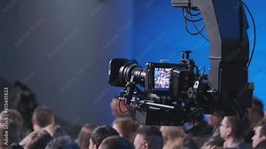 A professional video camera records a live event, focusing on the crowd and stage with a high-quality lens and advanced technical setup.