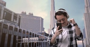 「都会で働くビルの前に立ちながらスマートフォンを使う、ヘッドホン付きのアジア男性フリーランサー」の動画素材（ロイヤリティフリー）1106091701 | Shutterstock