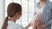 Doctor examining pregnant woman holding stethoscope near big belly...
