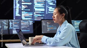 Side View Of Asian Female Programmer Thinking About Something While Writing Code By A Laptop Using Multiple Monitors Showing Database On Terminal Window Desktops In The Office