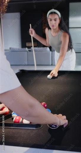 Vertical video: Two women prepping break at home pool table near racking balls while far lining cue