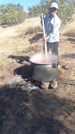 Outdoor Cooking: Stirring a Large Metal Pot Over Fire