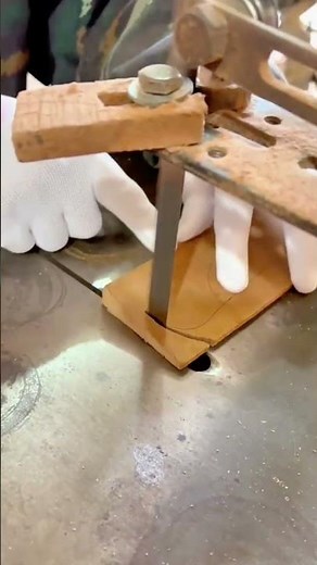 A craftsman cuts a small wooden piece into a curved shape using a coping saw
