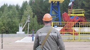 Slow motion shot of oil worker walking near oil pump jacks in oil field. Balancing drive rod pumps oil rocker. Pumping crude oil for fossil fuel energy with drilling rig in oil field.