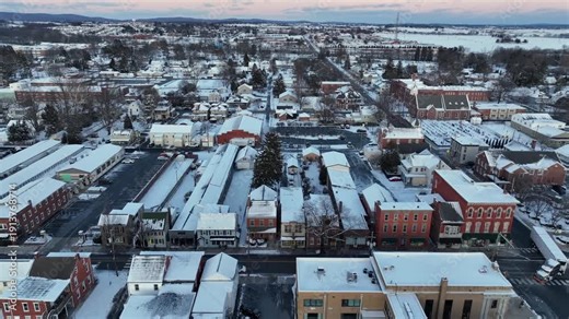 Historic residential district in Manheim, Pennsylvania covered in fresh snow during winter with small town streets and classic brick buildings. Slow drone flyover shot at sunrise.
