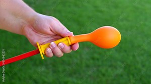 Woman inflating an orange balloon with a hand pump in slow motion. Green grass in backgroundd. Close up shot.