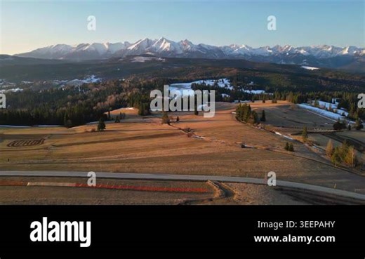 Aerial panoramic view of a rural countryside with fields and meadows stretching beneath snowy Alpine mountains. Early spring morning light and a clear blue sky at sunrise create a peaceful and Stock Video Footage - Alamy