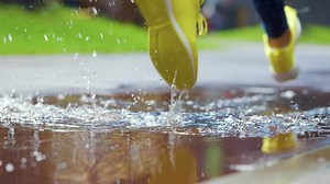Female sports woman jogging outdoors, stepping into puddle. Single runner running in rain, making splash. Slow motion