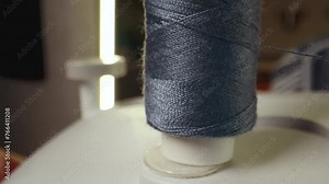Blue cotton spool thread unwinds on a sewing machine. Spinning roll of threads spins. Close up, selective focus. Needlework and handmade patchwork hobby.