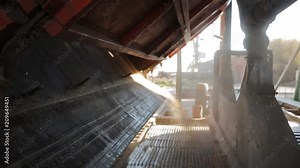 Close view of unloading grain trucks at elevator on elevating hydraulic platform unloader. Grain crops transshipment at big sea terminal at seaport. Grain is pouring down to silo.