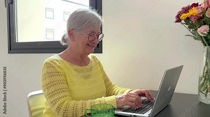 Relaxed attractive senior woman working on computer typing and smiling, white haired lady creates story or novel with laptop enjoying technology and social media