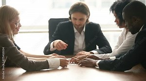 Multi-ethnic business group assembling jigsaw puzzle together at conference table, company leader helping team in decision making, teambuilding activity, contribution in common goal, teamwork support