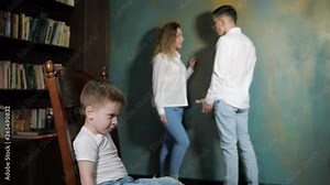 Couple of parents arguing in front of their kid. Sad little boy is listening his parent's shouting on each other, sitting on the chair, side view.