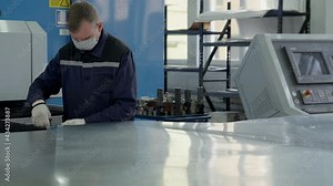 Inside a manufacturing facility. The operator is using a pliers tool. He takes the sheet and bends its corners, the places it on the side. Conveyor Machine.Production process.Operator in uniform