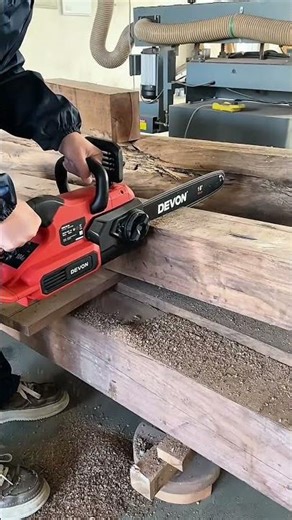 Operating a powerful red electric chainsaw to cut through a thick piece of solid timber wood