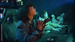 Medium angle shot of young Asian female gamer and diverse team mates playing intense match in shooter video game in cyberclub, loosing, taking off headsets and leaning back in chairs