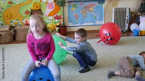 Children have fun sit and jump on large rubber inflatable balls in playroom
