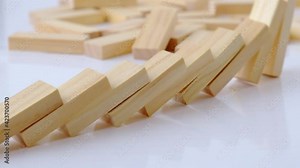 Domino effect, row of wooden domino falling down on white background. Dominoes falling in a row, hand pushes a Domino and starts a chain reaction Board game. Falling dominoes