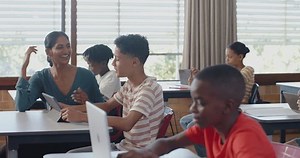 In school, students using laptops and tablets in classroom with teacher assisting. Education, technology, learning, digital, academic