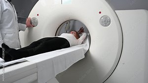 Young woman is undergoing a CT scan procedure. Pretty female in a modern laboratory, lying on the table during CT or MRI. Radiologist with a female patient in the room of computed tomography.