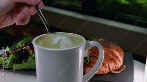 Waiter puts hot matcha tea with green foam on table. Alternative to cappuccino to reduce your caffeine intake and replace it with healthier macha tea. Consumption of Japanese macha tea by vegetarians